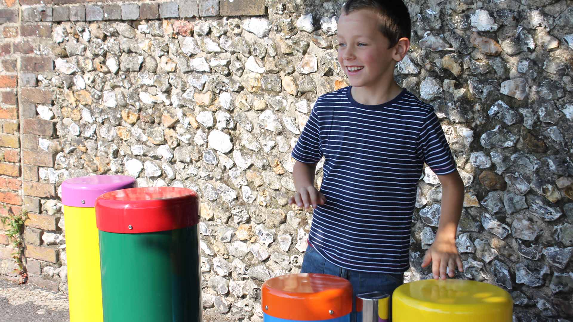 A child playing with coloured outdoor musical drums beside a flint wall
