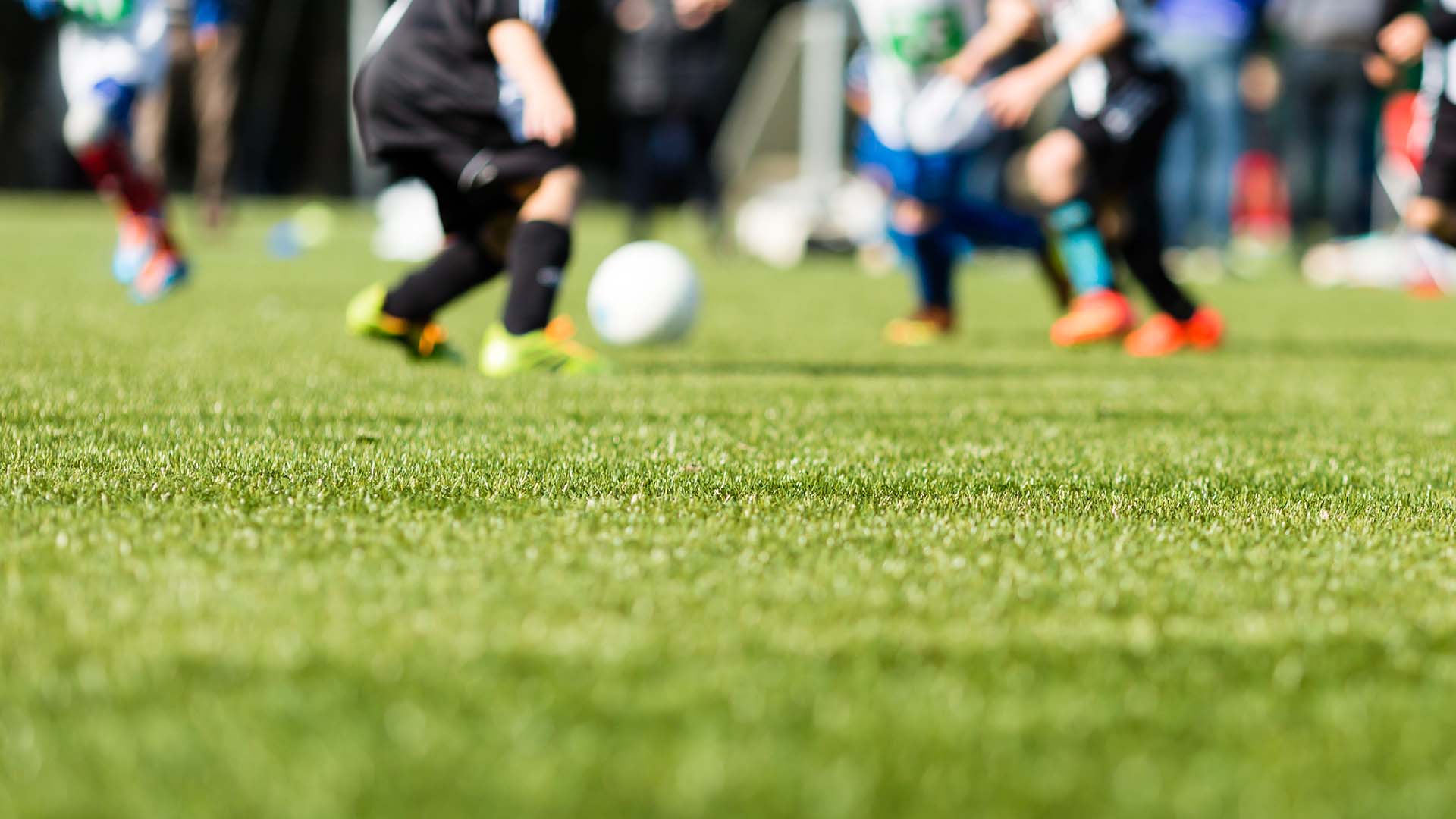 Children playing football on an artificial grass pitch, seen at ground level