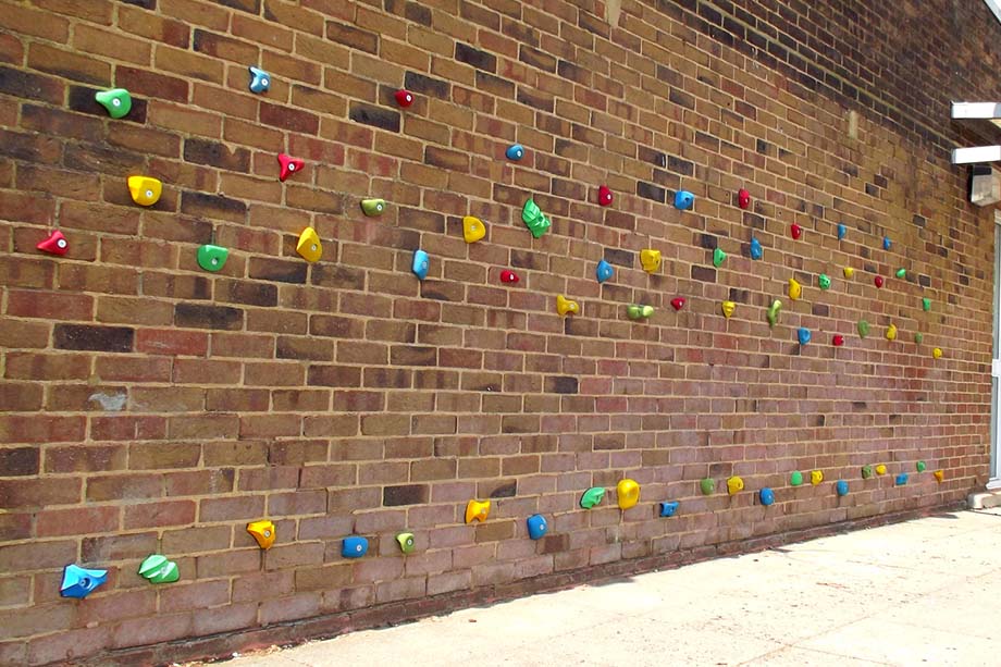 Traverse climbing wall with coloured holds fixed to a school brick wall
