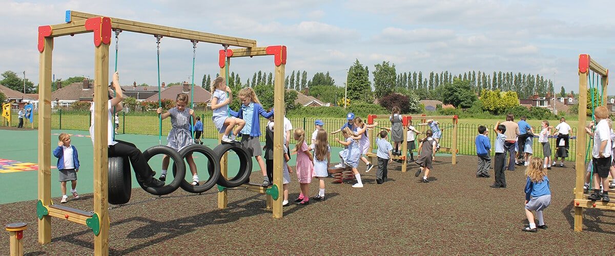 A trim trail on a school field, with hanging tyres and timber climbing frames
