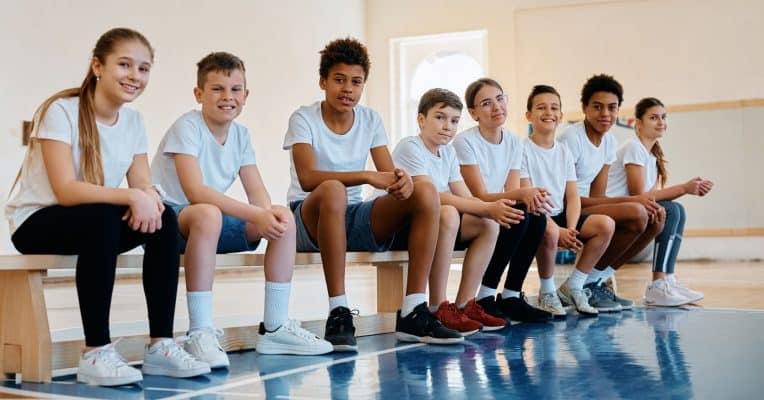 Students sitting on a balance bench in a school sports hall