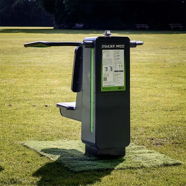 Outdoor shoulder press machine in a park on a grassy field. Sunlight casts soft shadows, creating a serene, inviting atmosphere.